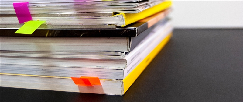 A stack of bound reports with stickers coming out of the book. Photo by Bernd Klutsch via Unsplash.